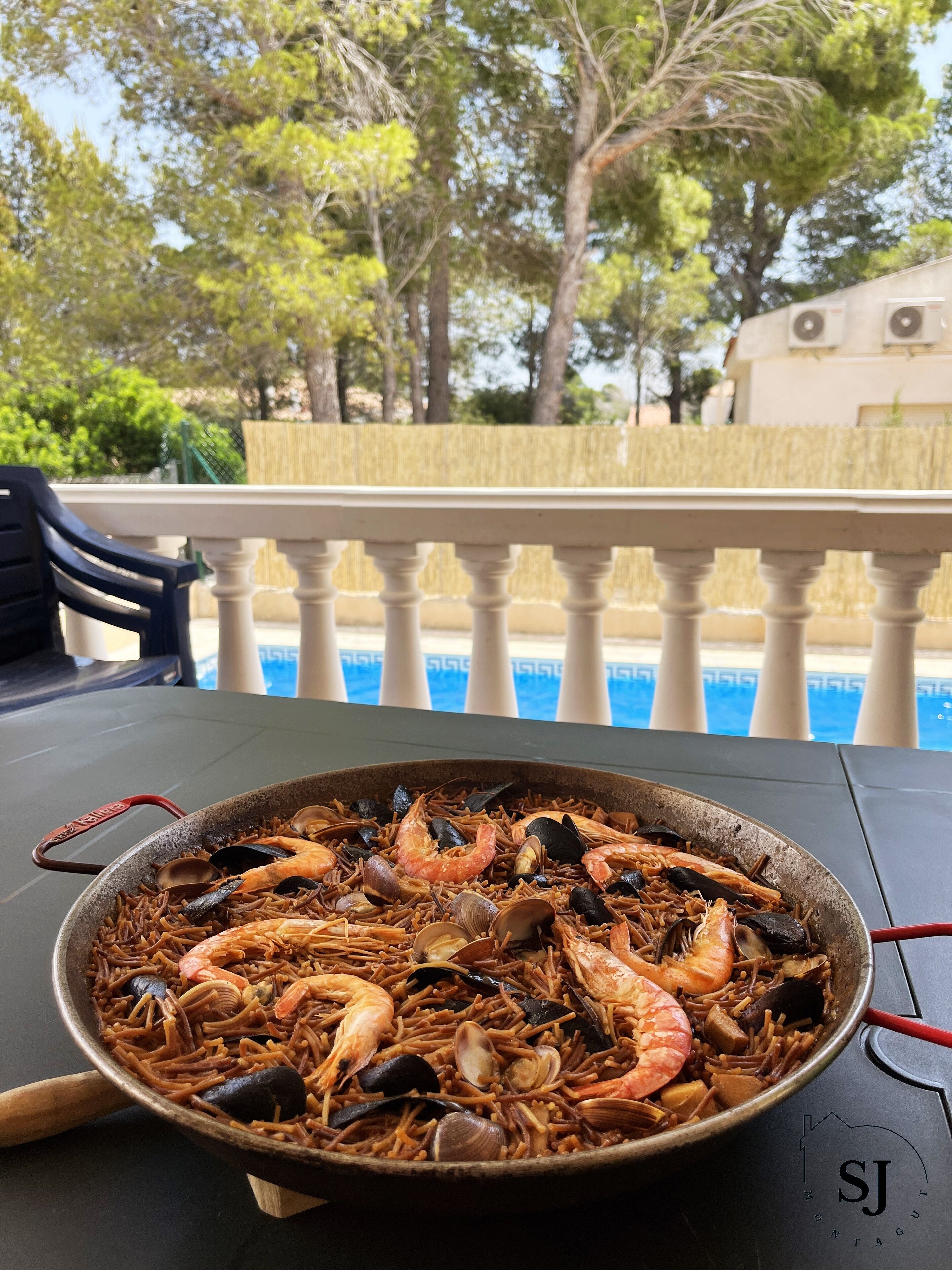 Una paella de mariscos sobre una mesa con vista a la piscina.