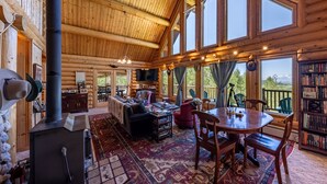 A log cabin interior with a fireplace, a dining area, and large windows offering a view of the outdoors. - Beautiful Moran Home with spectacular Teton Views (Moran)