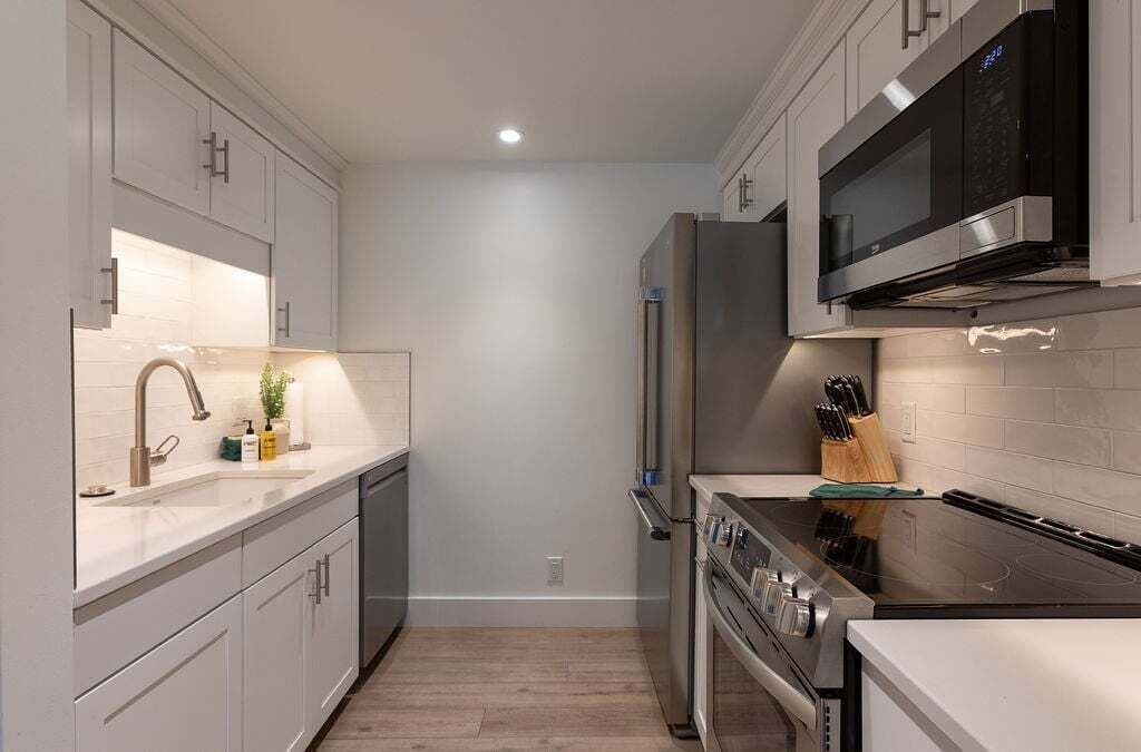 Une cuisine moderne avec des meubles blancs, des appareils en acier inoxydable et un four à micro-ondes placé au-dessus de la cuisinière.
