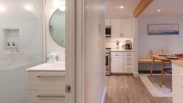 Une cuisine moderne avec des meubles blancs, un miroir rond et un coin repas comprenant une table et un banc en bois.