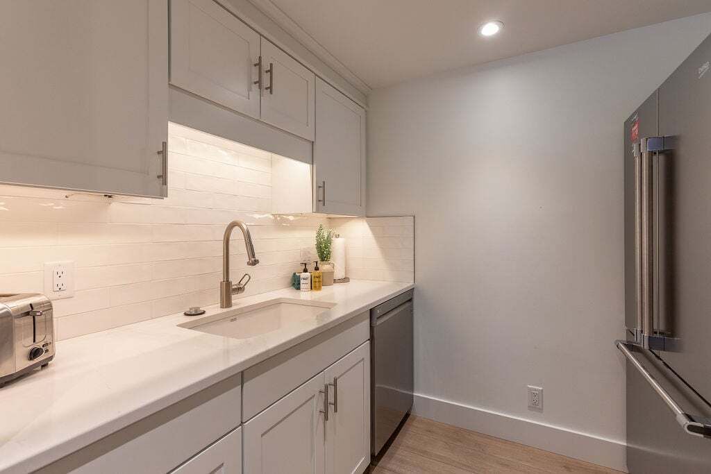 A modern kitchen with white cabinetry, a stainless steel refrigerator, and a built-in dishwasher.