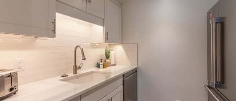 A modern kitchen with white cabinetry, a stainless steel refrigerator, and a built-in dishwasher.