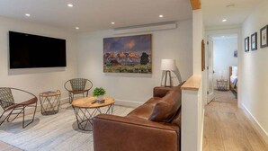 Un salon moderne avec un canapé en cuir marron, deux fauteuils à motifs, une table basse ronde et un téléviseur à écran plat fixé au mur.