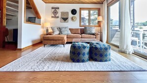 A cozy living room with a wooden ceiling, a sofa, patterned cushions, a coffee table, and a large window with a view. - Modern Mountain Townhome with Mountain Views! (Mount Crested Butte)