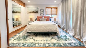 A bedroom with a bed, two bedside tables, a window with blinds, a mirror, and a wall-mounted artwork. - Modern Mountain Townhome with Mountain Views! (Mount Crested Butte)