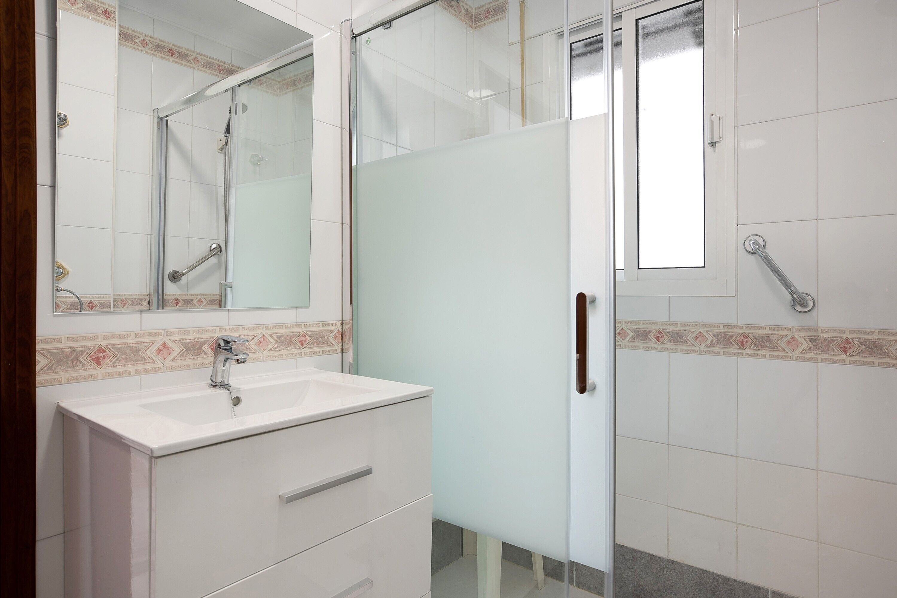 A bathroom with a white sink, a mirror, a glass shower enclosure, and a door with a handle.