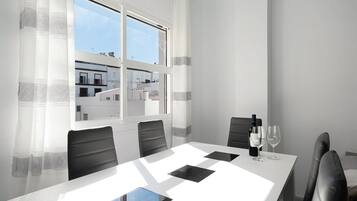 A modern dining room with a white table, black chairs, and a view of buildings through a window.