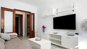 A modern living room with a sofa, TV, white entertainment unit, and a door leading to another room. - Apartment 'Romo' close to the Beach with Balcony & Wi-Fi (conil de la frontera)