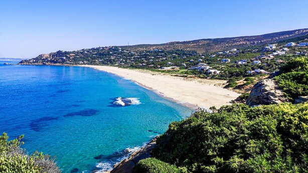 A coastal landscape with a sandy beach, clear blue sea, and a hillside with scattered buildings. - Apartment 'Romo' close to the Beach with Balcony & Wi-Fi (conil de la frontera)
