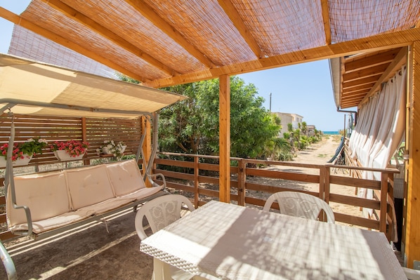 Un espace extérieur abrité, avec une table et des chaises, une clôture en bois et des plantes en pot.