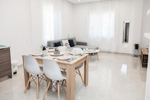 Uma sala de estar moderna com um sofá cinzento, uma mesa de jantar com cadeiras e uma mesa de centro.