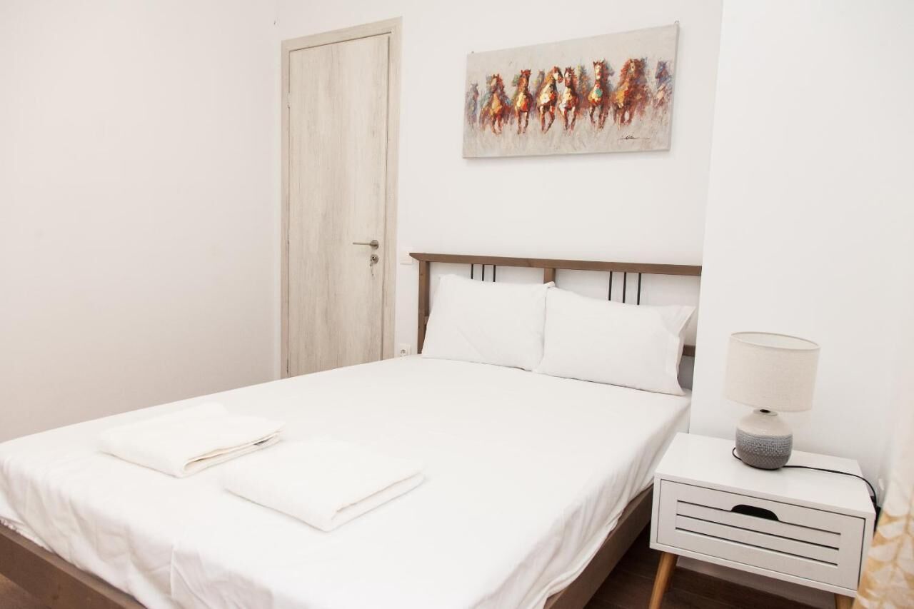 A neatly made bed with white linens and pillows, a bedside table with a lamp, and a door to the left.