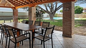 Een buitenpatio met een houten pergola, een bakstenen pilaar en een zwembad op de achtergrond.