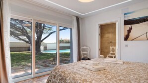 Een slaapkamer met een groot bed, een stoel, een schilderij en uitzicht op een zwembad.