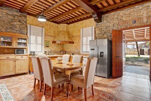 Uma cozinha com mesa de jantar, cadeiras, geladeira e parede de pedra.