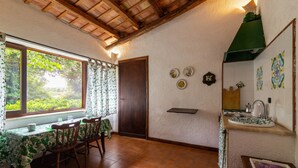 A dining area with a table and chairs, a window with curtains, a door, and a kitchen area with a sink and tiles. - Apartment 'Tenuta Donna Vittoria Edera' with Mountain View, Wi-Fi and Air Conditioning (Trapani)