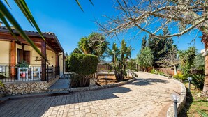 Un camino pavimentado que conduce a un edificio con un muro de piedra y una pérgola de madera.