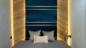 Una cama con un colchón gris, dos almohadas y un cojín decorativo con contorno dorado.