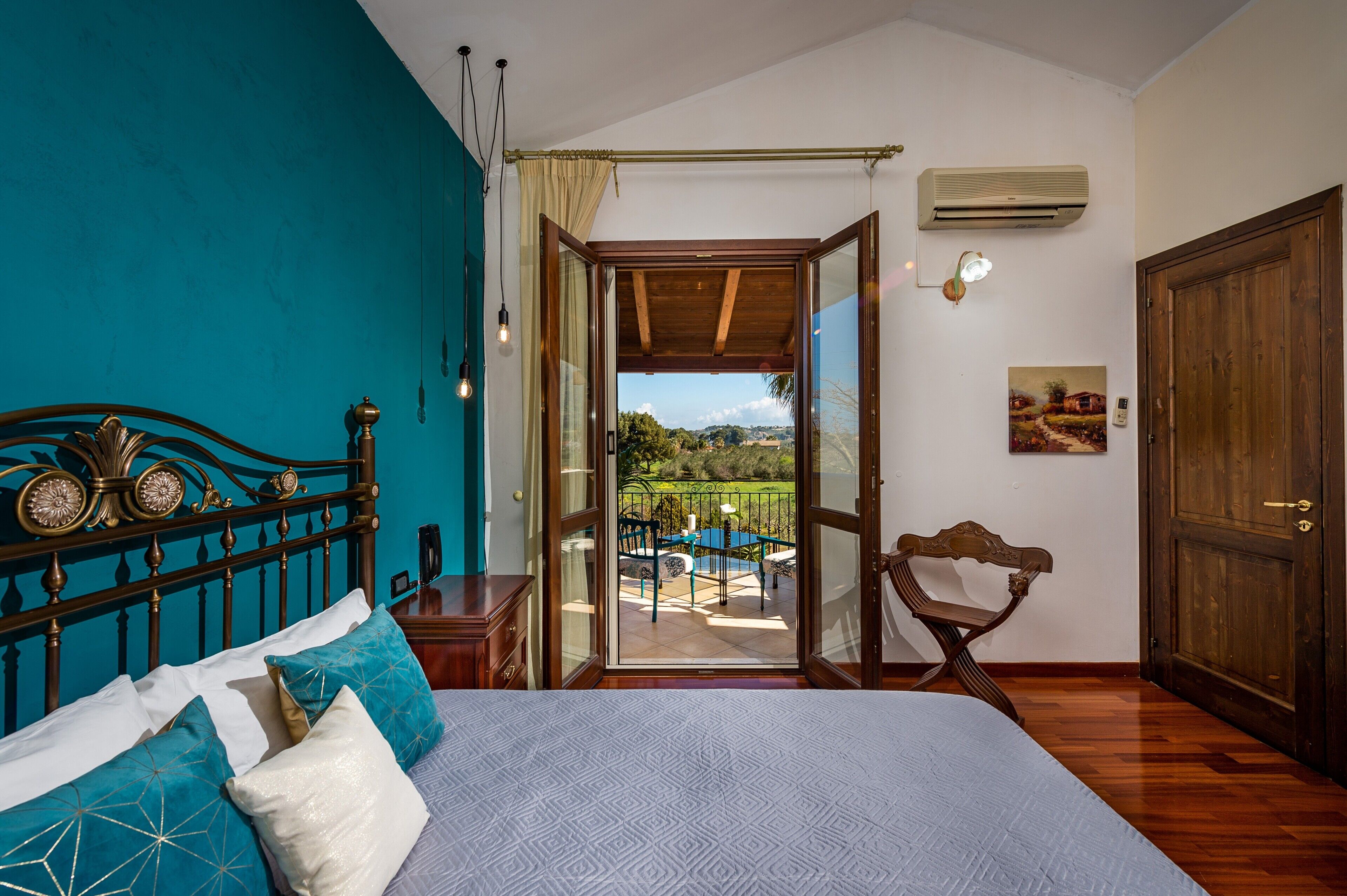 Un dormitorio con cama, cabecera de madera, vista a un balcón y puerta que da al exterior.