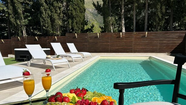 Un área junto a la piscina con una mesa dispuesta con fruta y bebidas, sillas de descanso y una valla de madera.