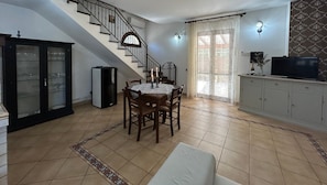 Un espace repas comprenant une table et des chaises, un escalier, un meuble et un téléviseur.