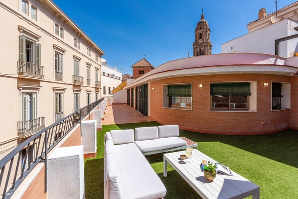 A courtyard with a white sofa, a table with a plant, and a view of a bell tower.