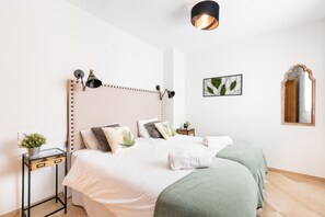 A bedroom with a bed, bedside tables, a wall-mounted lamp, a framed picture, and a mirror.