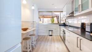 Une cuisine moderne avec des meubles blancs, un plan de travail noir, des tabourets en bois et une fenêtre donnant sur un immeuble.