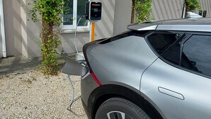 Um carro prateado estacionado em frente a um prédio com pérgola de madeira, uma janela e uma estação de carregamento identificada como "chargepoint+".