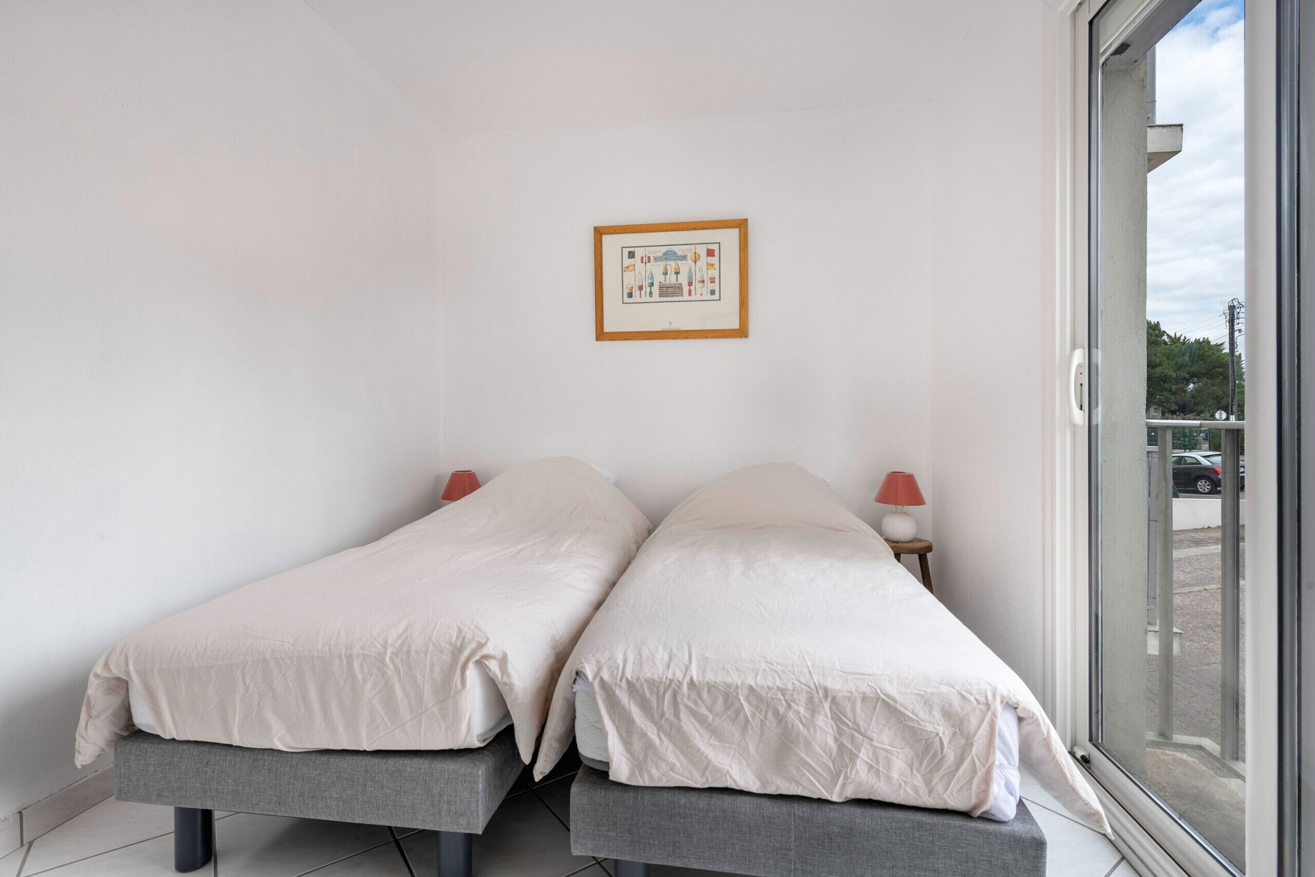 A bedroom with two beds, a framed picture on the wall, and a window with a view of the outside.