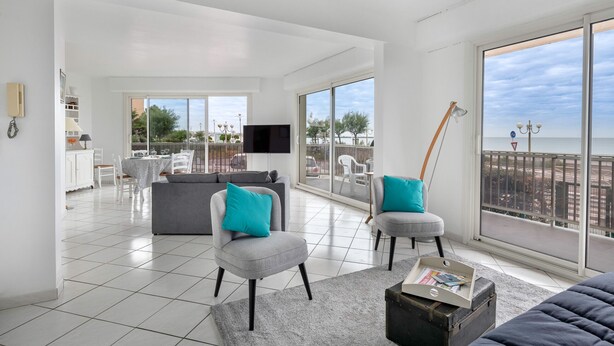 A spacious living area with a grey sofa, two armchairs, a dining table, and a TV. Large windows offer a view of the sea and a balcony. - Seafront, beautiful apartment for 4 with terrace (La Baule-Escoublac)