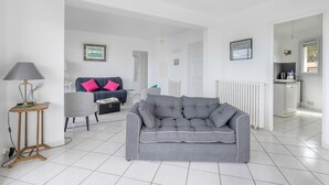 A modern living room with a grey sofa, a small side table, and a lamp. There is a kitchen area visible in the background. - Seafront, beautiful apartment for 4 with terrace (La Baule-Escoublac)