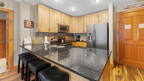A modern kitchen with wooden cabinets, a granite countertop, stainless steel appliances, and a bar stool seating area. - River Run Condo with Mountain Views from Private Balcony & Close to Shops! (Keystone)