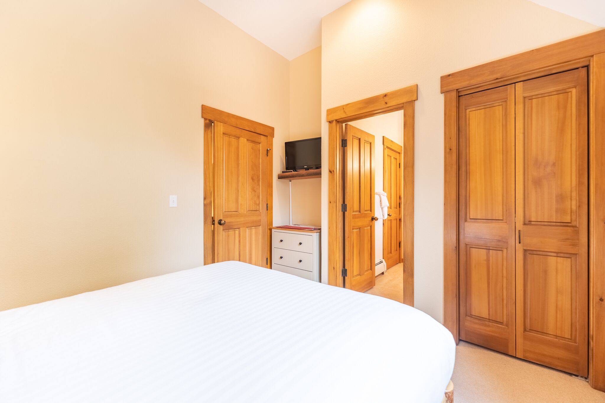 Une chambre à coucher avec un lit, des armoires en bois, une petite table de chevet et un téléviseur posé sur une étagère.