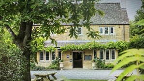 A stone building with a tiled roof, a central door, and a small garden area with a picnic table. - The Vines (Bampton)