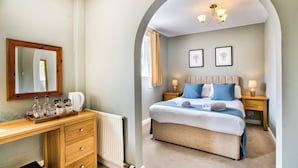 A hotel bedroom with a large bed, a wooden dresser, a mirror, and two bedside lamps. - The Vines (Bampton)