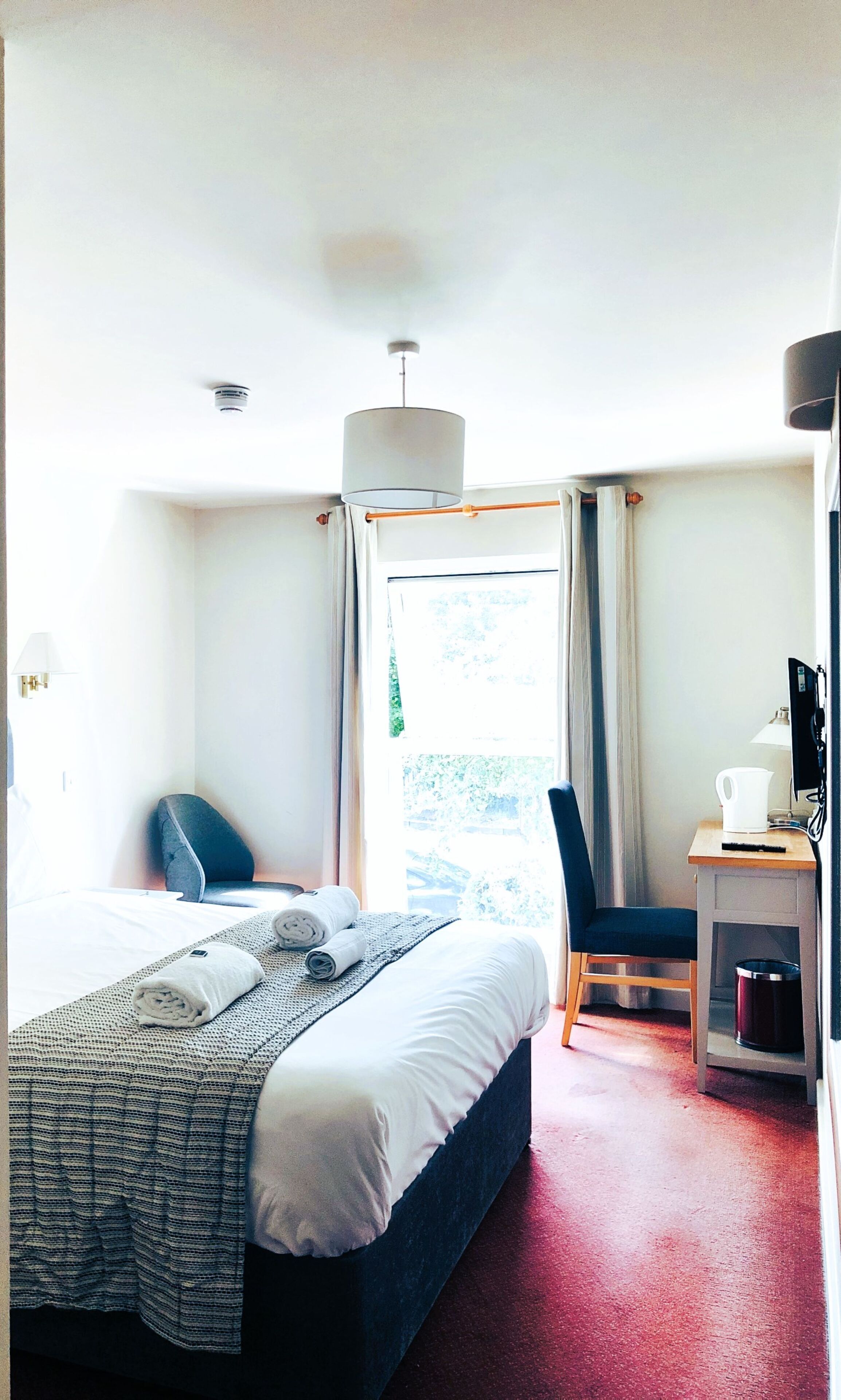 Een hotelkamer met een bed, een bureau met een computer, een stoel en een raam met gordijnen.