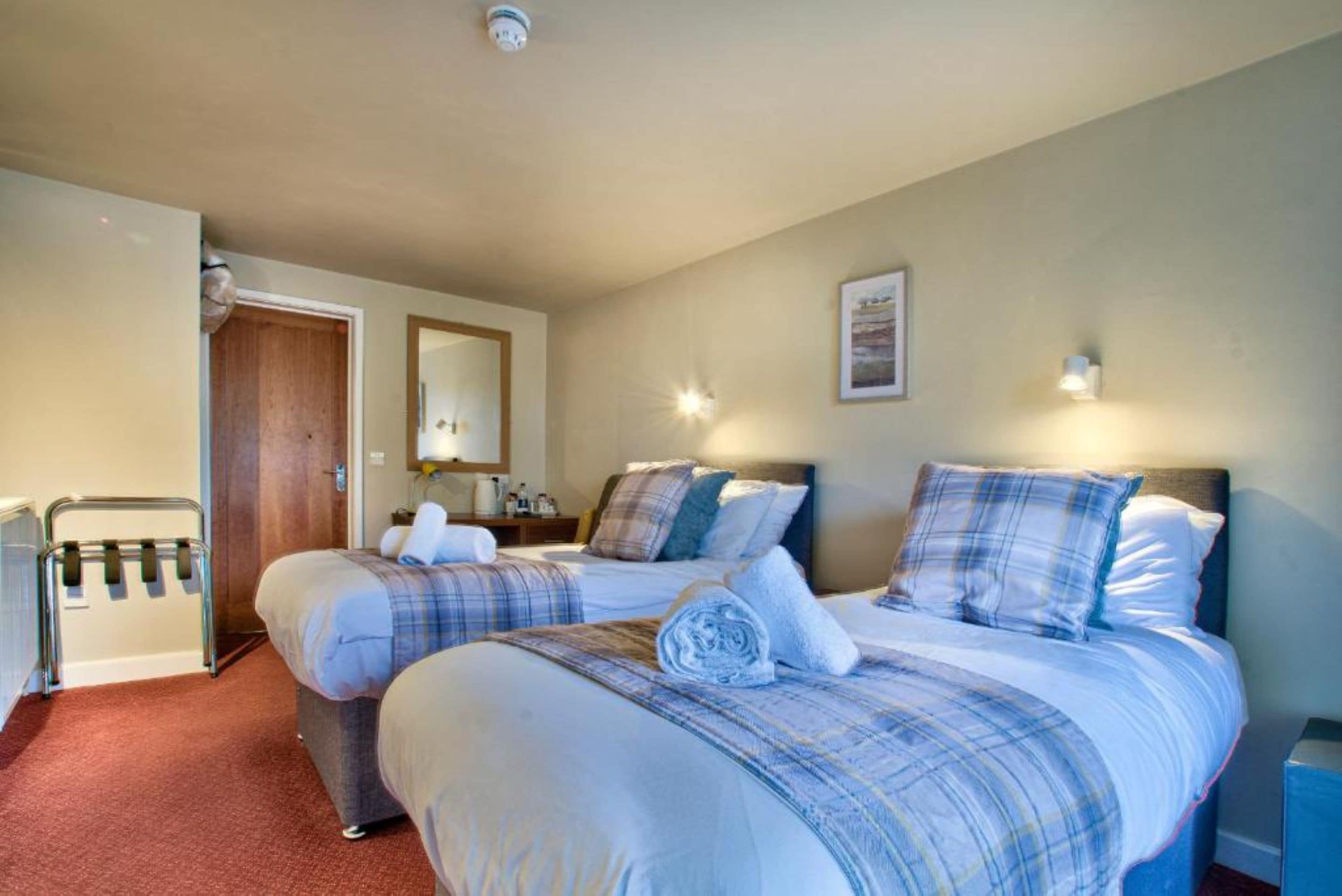 Habitación de hotel con dos camas, una puerta de madera, un radiador y una lámpara fijada a la pared.