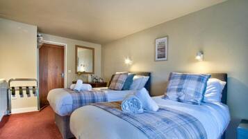 Habitación de hotel con dos camas, una puerta de madera, un radiador y una lámpara fijada a la pared.