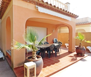 Ein möblierter Patio mit Tisch, Stühlen, Topfpflanzen und einer Liege.