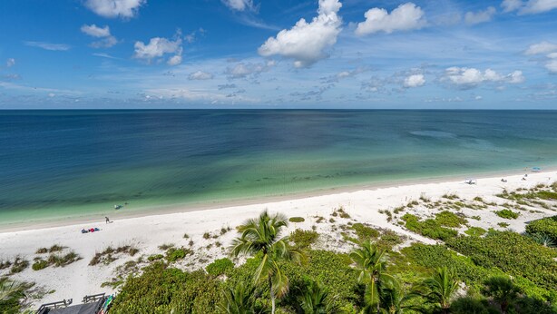 Ein Strand mit klarem türkisblauem Wasser, weißem Sand und vereinzelten Palmen.