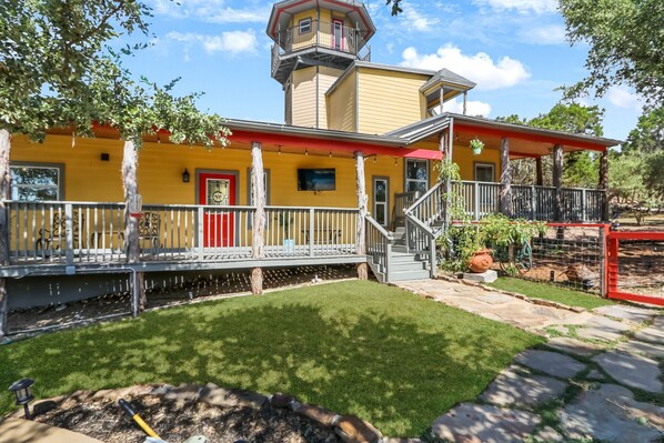 A yellow building with a red door, a balcony, and a tower.