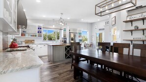 Una cocina moderna con armarios blancos, una mesa de comedor de madera y vistas al exterior.