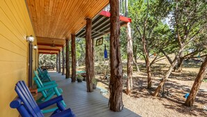 Una terraza de madera con sillas azules, un área cubierta con techo de madera y árboles al fondo.