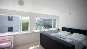 A bedroom with a bed, a window, and a view of buildings and greenery.