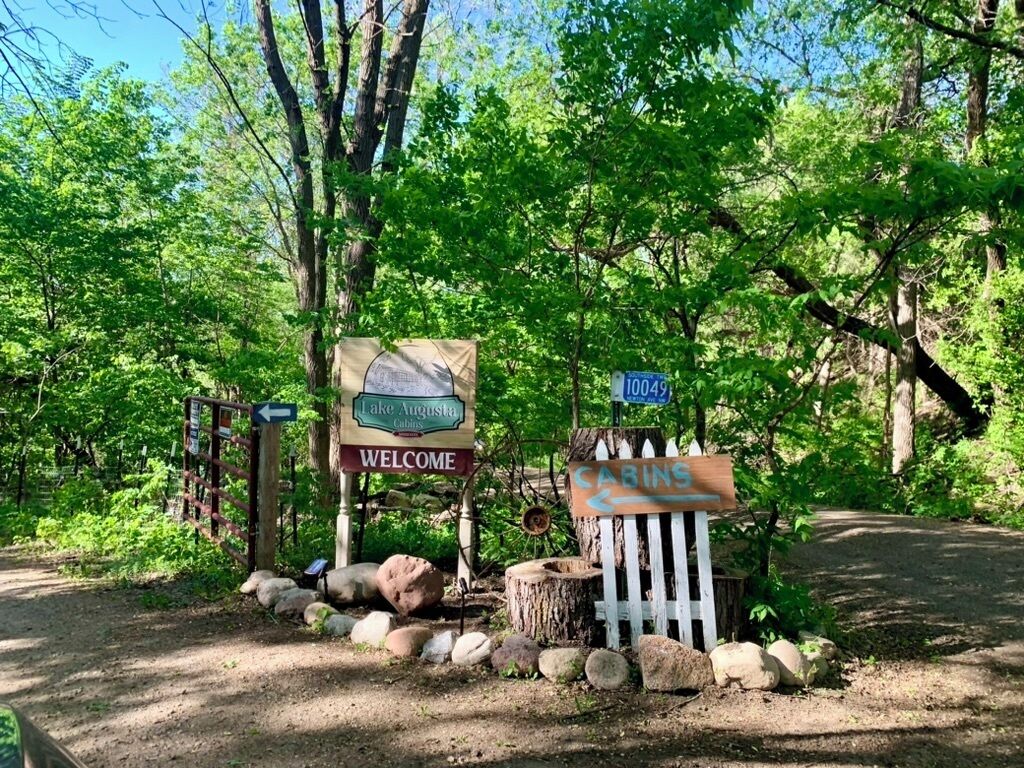 A welcome sign for Lake Augusta Cabins, a trail sign, and a wooden cabin sign.