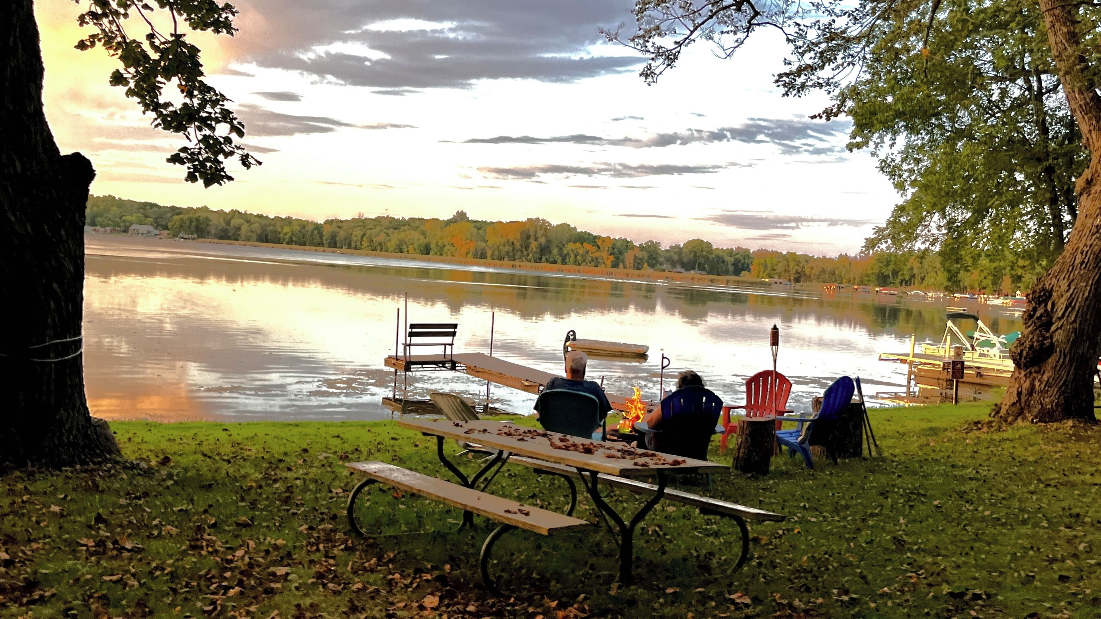 A lakeside picnic setup with a table, chairs, and a fire pit.