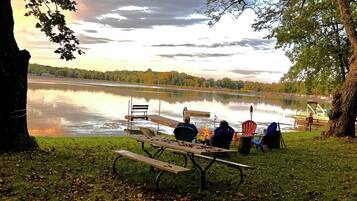 A lakeside picnic setup with a table, chairs, and a fire pit.