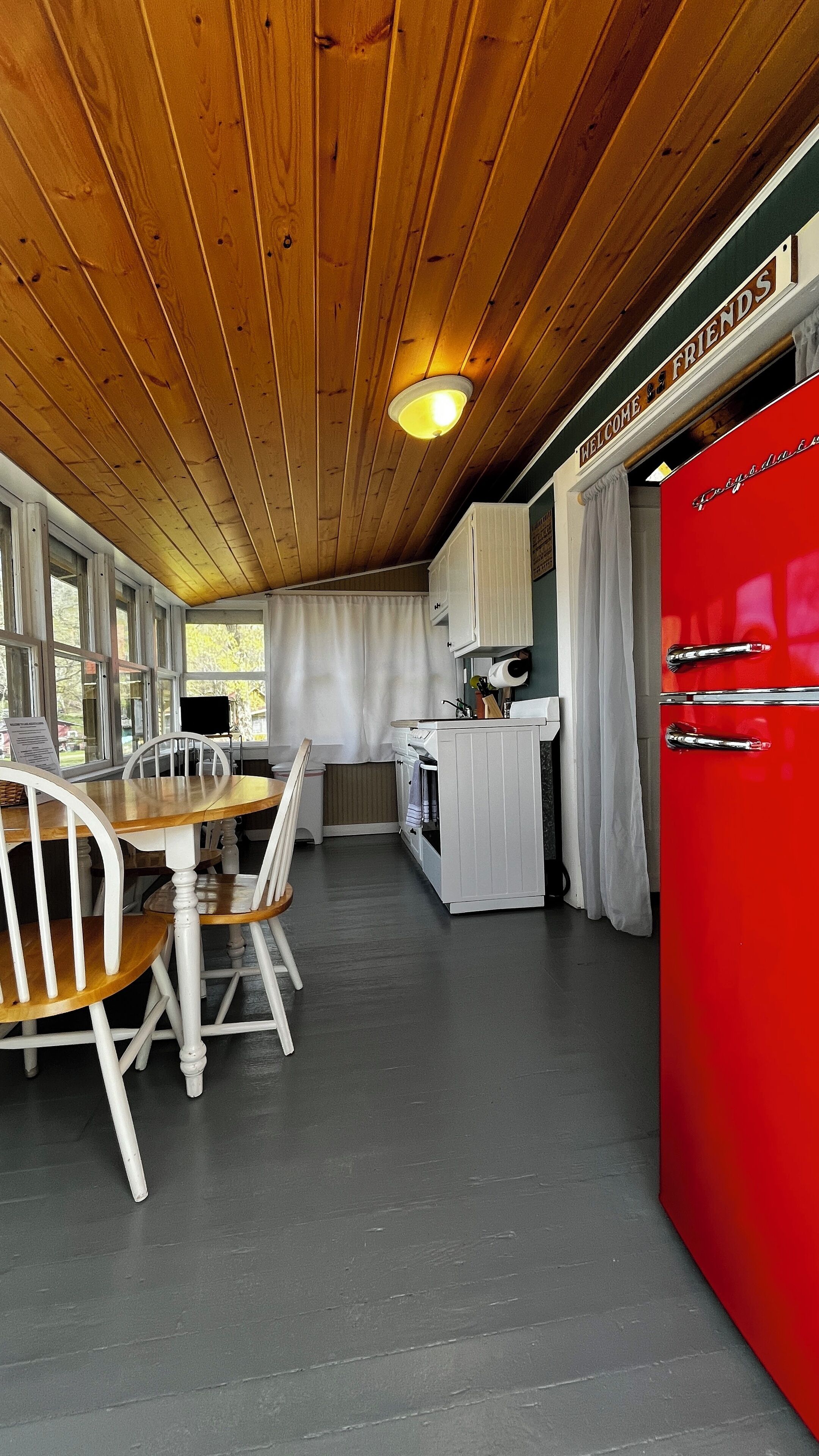 A compact kitchen with wooden ceiling, a red refrigerator, white cabinets, and a dining area with a wooden table and chairs.