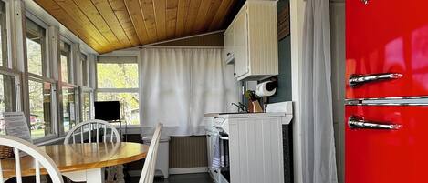 A compact kitchen with wooden ceiling, a red refrigerator, white cabinets, and a dining area with a wooden table and chairs.